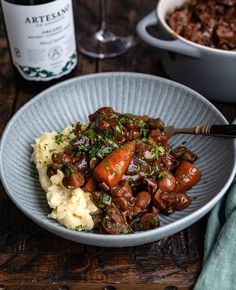 a plate with mashed potatoes, meat and gravy next to a bottle of wine