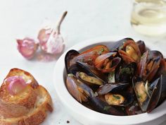 a bowl of mussels next to some bread