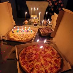 three pizzas with candles on them sitting in boxes next to some cupcakes