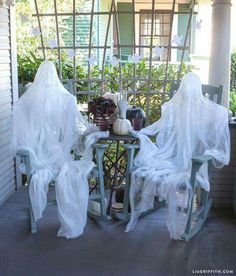 two chairs covered in white plastic sitting on a porch next to a table and potted plants