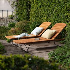 two wooden chaise lounges with pillows on them in the middle of a garden