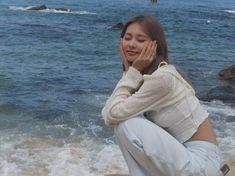 a woman sitting on the beach with her hands to her face