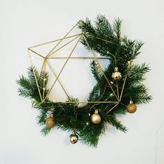 a christmas wreath with ornaments hanging from it's sides on a white wall next to a gold star ornament