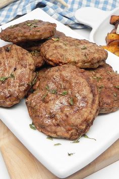 several hamburger patties on a white plate next to grilled potatoes and carrots