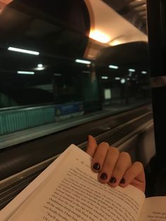 a woman's hand holding an open book in front of her face while riding the subway