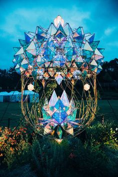 an artistic sculpture in the middle of a garden at night with blue sky and clouds behind it