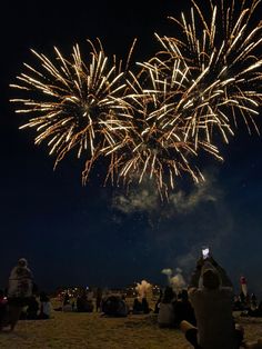 people are sitting on the beach watching fireworks