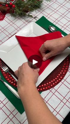 a person is cutting out a red napkin on a white plate with silverware in it