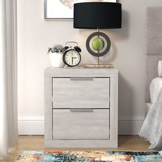 a nightstand with two drawers and a clock on it next to a bed in a bedroom