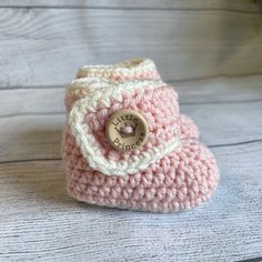 a pink crocheted boot with a button on the side sitting on a wooden surface