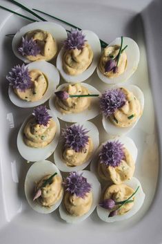 an assortment of deviled eggs with flowers in them on a white platter, ready to be eaten