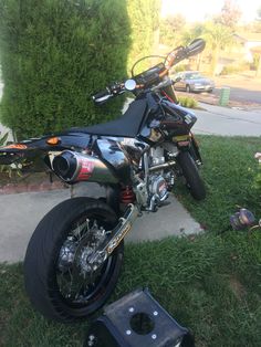 a motorcycle parked on the side of a road next to some bushes and flowers in front of a house