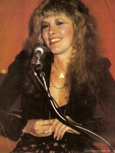 a woman sitting in front of a microphone with long hair and wearing a black dress