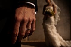 a man and woman standing next to each other in front of a wall wearing wedding rings