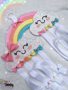 two white hair clips with rainbows and clouds on them, one has a pink bow