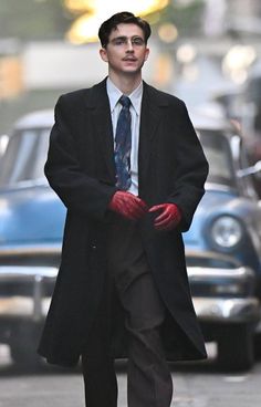 a man in a suit and tie is walking down the street while wearing red gloves