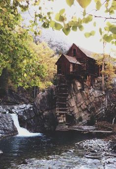 an old water mill sits on the edge of a river with a waterfall running through it