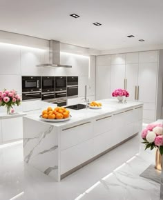 a white kitchen with marble counter tops and an island that has fruit on it in the center