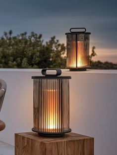 two outdoor lanterns sitting on top of a wooden block next to a chair and table