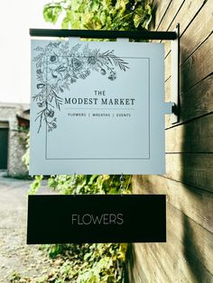 a sign hanging from the side of a wooden building next to a fence with flowers on it