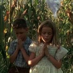 two children are praying in the middle of a cornfield