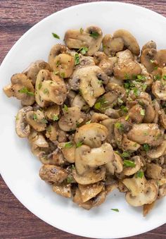 a white plate topped with mushrooms and parsley on top of a wooden table next to a fork