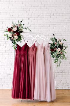 three bridesmaid dresses hanging on a rack in front of a white brick wall