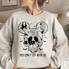 a woman wearing a mickey mouse sweatshirt with the words you can't sit with us on it