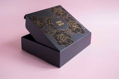 an open black box with gold flowers on the lid sitting on a pink table top