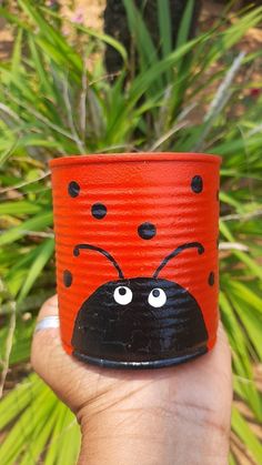 a hand holding a red and black cup with a lady bug painted on it