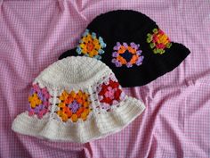 two crocheted hats laying on top of a pink blanket