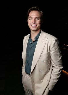 a man in a white suit and green shirt posing for the camera with his hands in his pockets