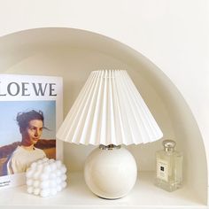 a white lamp sitting on top of a shelf next to a book