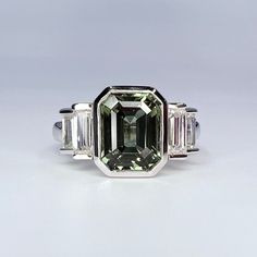 an emerald and diamond ring with three baguets on the side, set in white gold