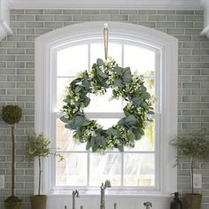 a wreath hanging from the window above a kitchen sink