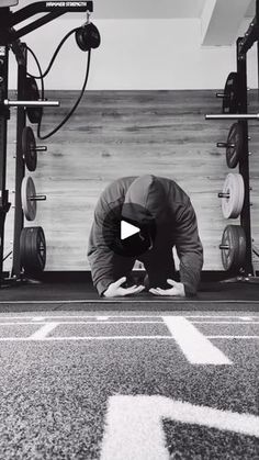 a man squats on the ground in front of a barbell rack