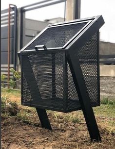 a black metal box sitting on top of a field next to some grass and dirt