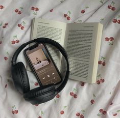 an open book and headphones are laying on a bed with cherry - patterned sheets