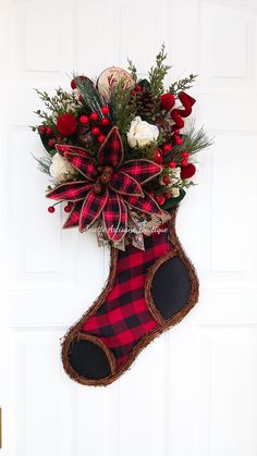 a christmas stocking hanging on the front door with flowers and greenery in it