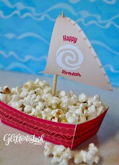 a small boat with a happy birthday sign on it is in a red box filled with popcorn