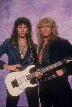 two people standing next to each other holding guitars