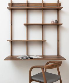 a wooden desk and chair in front of a white wall with shelves on the side