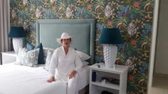 a woman sitting on top of a bed in a room with floral wallpaper and lamps