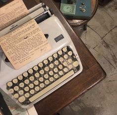 an old fashioned typewriter sitting on top of a wooden table next to a lamp