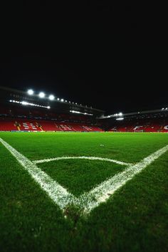 an empty soccer field at night with bright lights on the stadium's stands and green grass