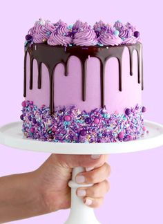 a person holding a cake with purple frosting and sprinkles on it