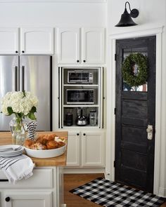 a kitchen with white cabinets and black door, flowers in a vase on the counter