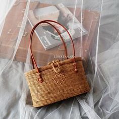 a straw bag sitting on top of a bed next to a book and magazine case