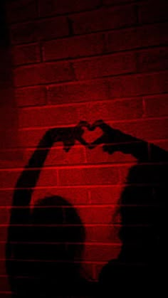 the shadow of a person making a heart with their hands in front of a brick wall