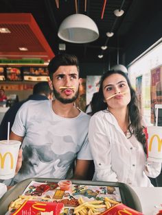 a man and woman sitting at a table with food in front of them, making funny faces